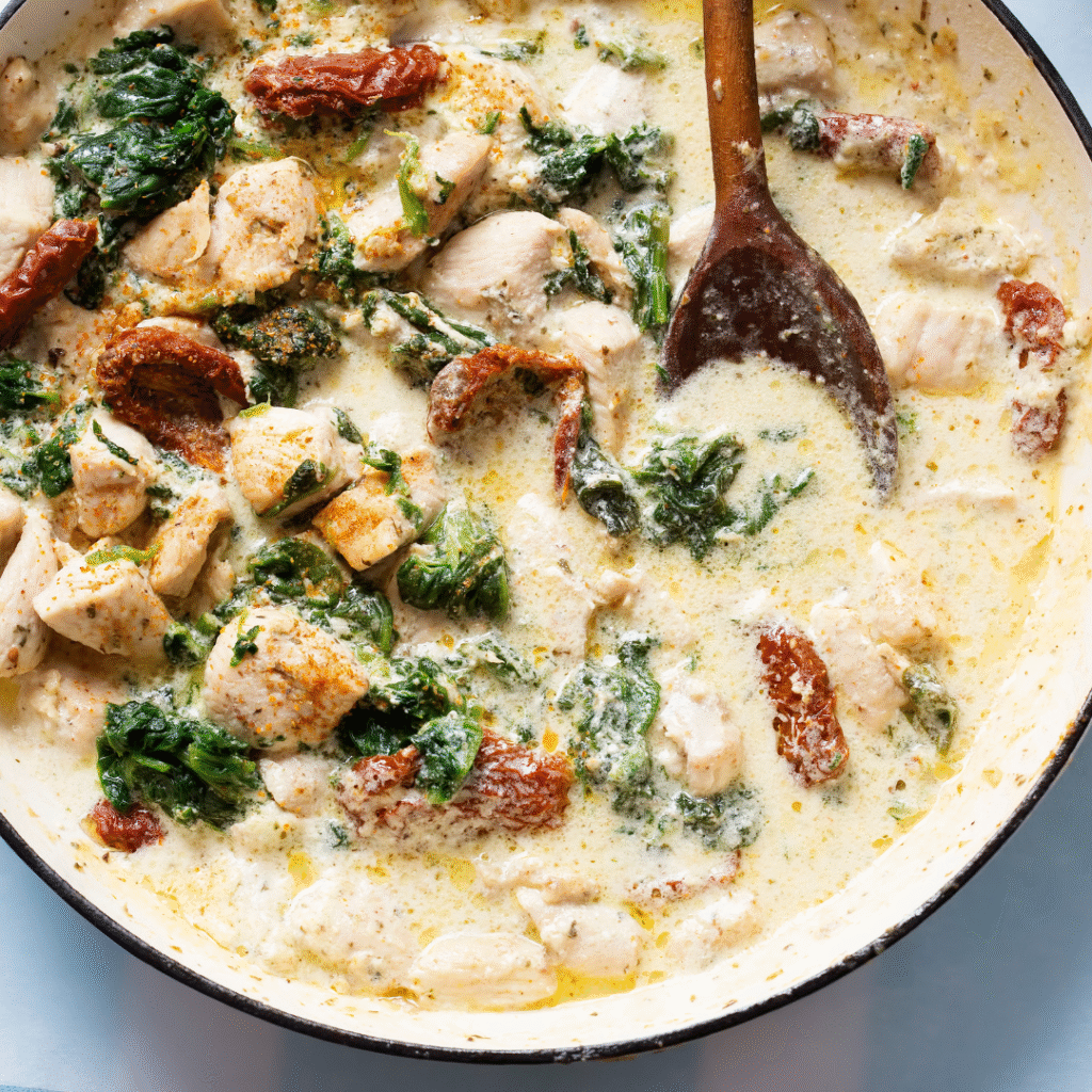 Close-up of a serving of Creamy Tuscan Chicken with tender chicken pieces, vibrant spinach, and sun-dried tomatoes in a rich, creamy sauce, garnished with fresh herbs, on a white plate