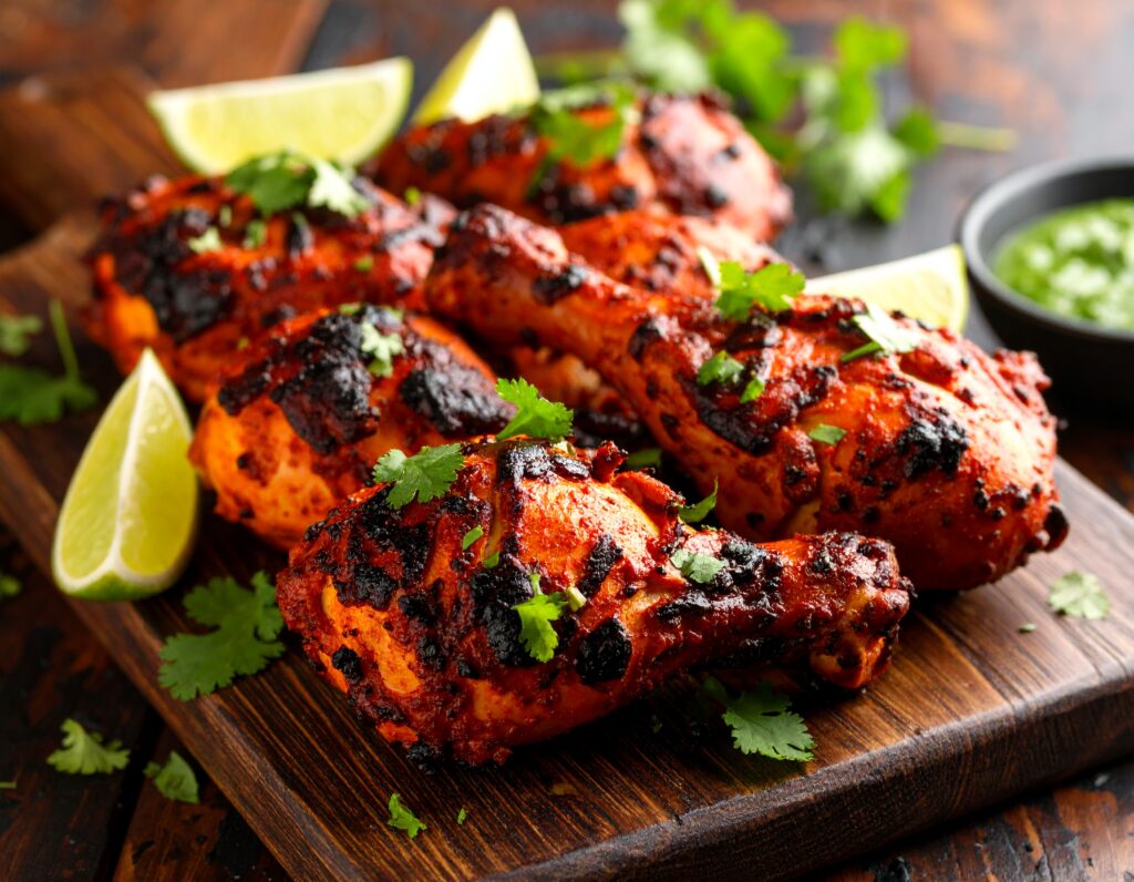 Pieces of vibrant red tandoori chicken, charred and juicy, served on a platter with fresh cilantro